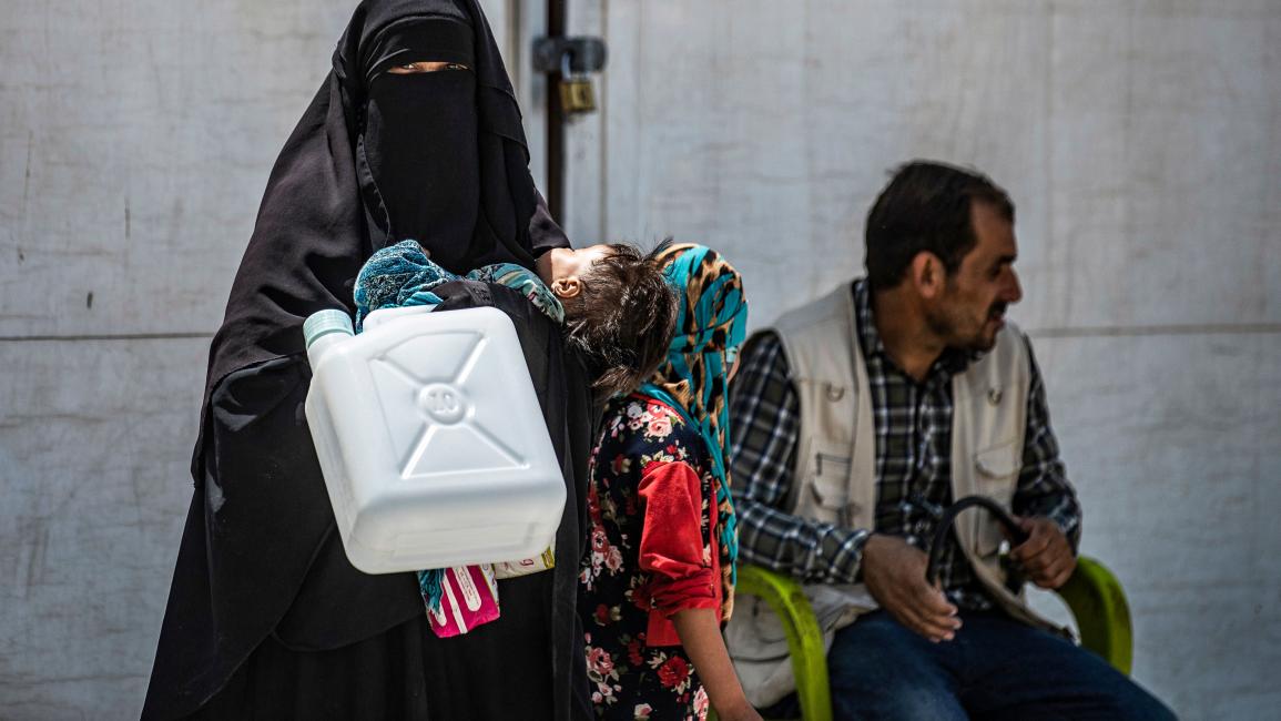 TOPSHOT-SYRIA-CONFLICT-DISPLACED-AID TOPSHOT - A woman wearing a niqab (full face veil) stands carrying a jerry can and a toddler at al-Hol camp for displaced people in al-Hasakeh governorate in northeastern Syria on July 22, 2019, as people collect UN-provided humanitarian aid packages. (Photo by Delil souleiman / AFP) (Photo credit should read DELIL SOULEIMAN/AFP via Getty Images)