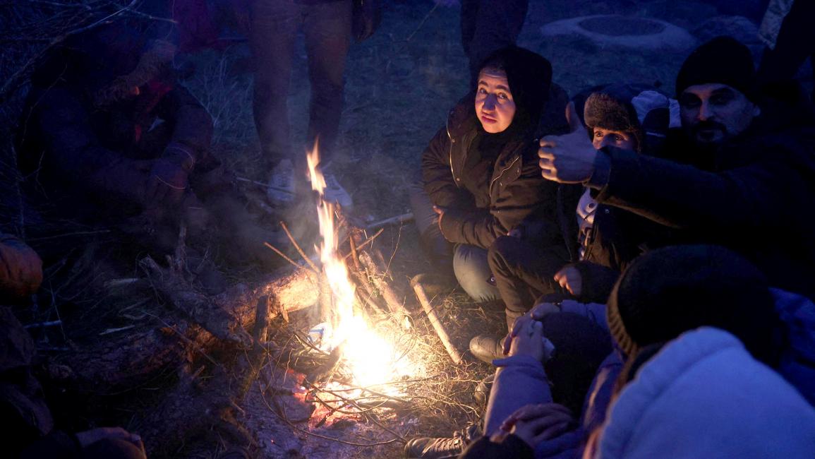 مهاجرون يشعلون ناراً لتحميهم من لسعات البرد القارص على الحدود البيلاروسية البولندية.