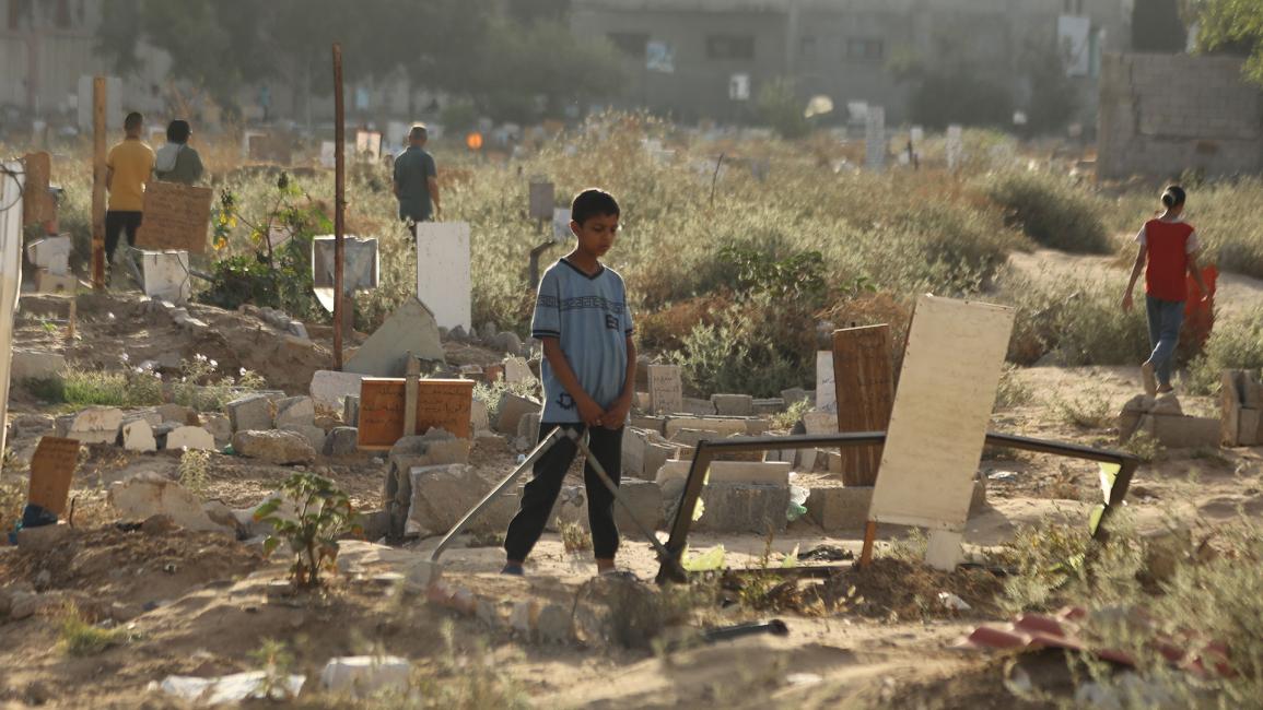طفل فلسطيني يقف أمام قبر لأحد أفراد أسرته (داود أبو الكاس/الأناضول)