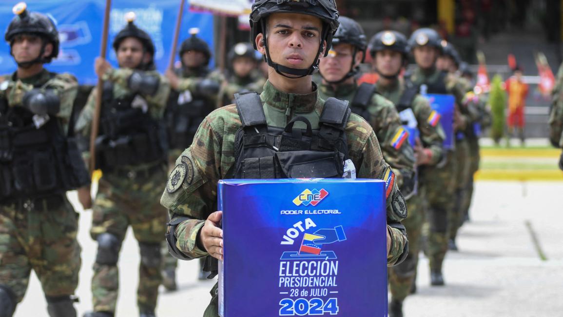 جندي يتقدّم آخرين يحملون صناديق الاقتراع في الانتخابات الرائسية المقبلة خلال عرض عسكري في كاراكاس (24/7/2024 فرانس برس)