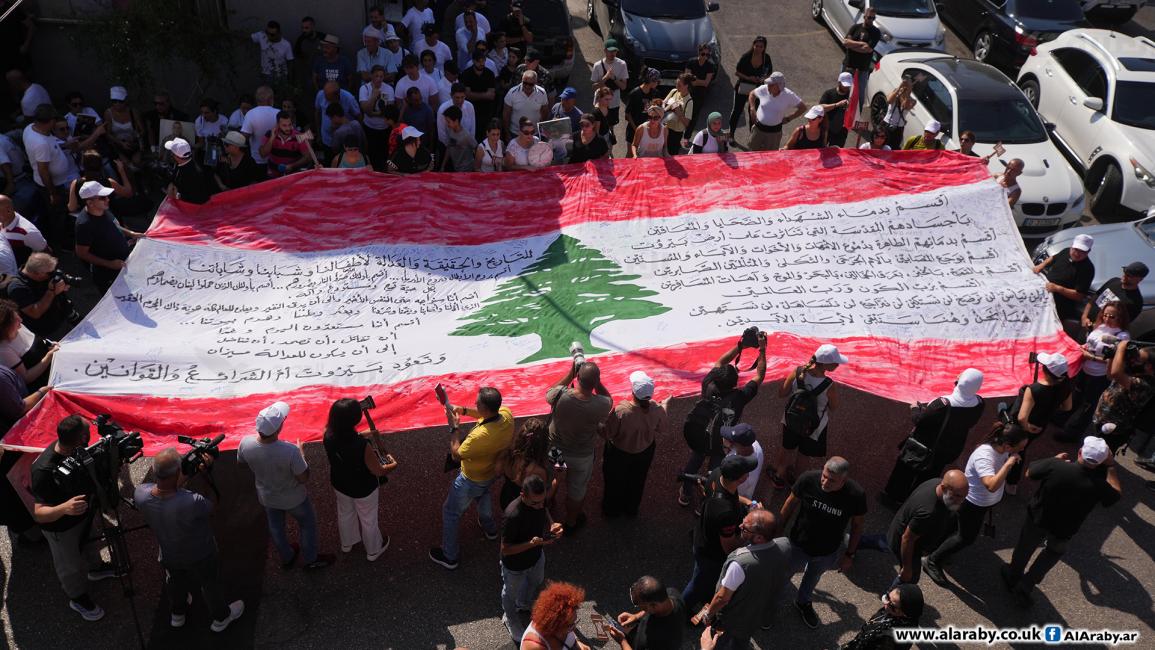 حمل المشاركون صور الضحايا وعلماً لبنانياً كبيراً يحمل عريضة موقعة من أهاليهم (حسين بيضون/العربي الجديد)
