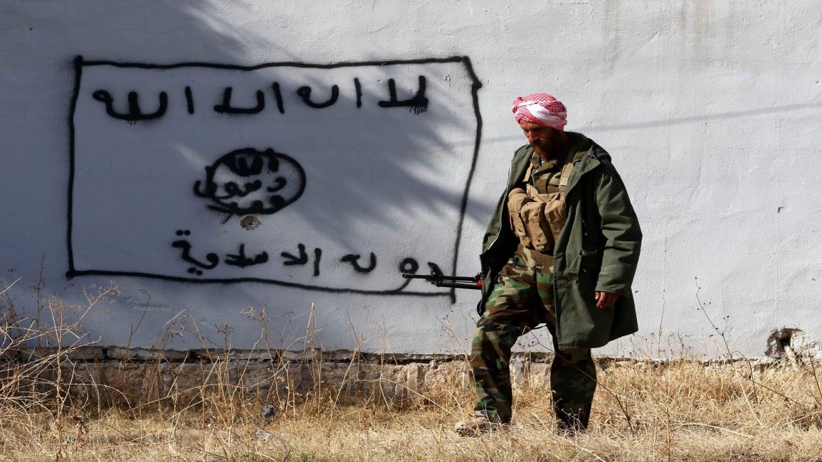 مقاتل كردي أمام حائط عليه شعار "داعش" (فرانس برس)