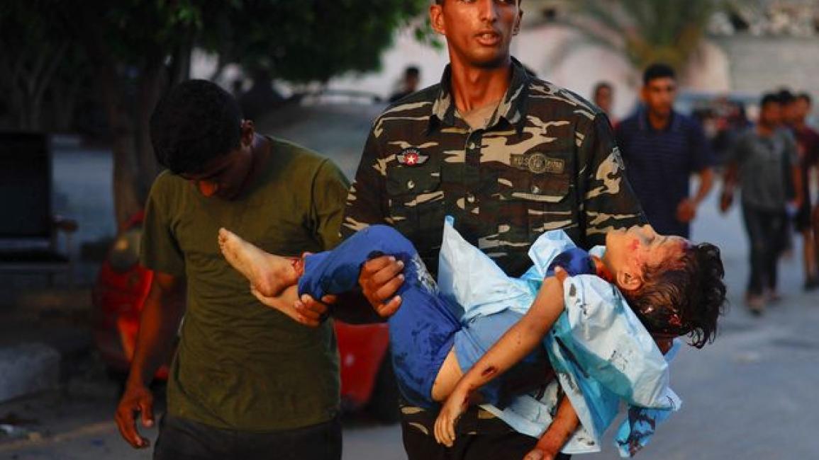 فلسطيني يحمل طفلا جريحا جراء قصف إسرائيلي على خانيونس (رويترز)
