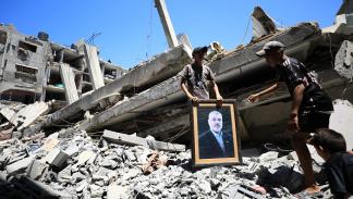 غزة | يحملان صورة هنية فوق الأنقاض في مخيم الشاطئ 31/7/2024 (داوود أبو الكاس/الأناضول)