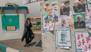 امرأة إيرانية أمام ملصقات انتخابية ومجسم لصندوق الاقتراع في طهران (20/ 6/ 2024 فرانس برس) 