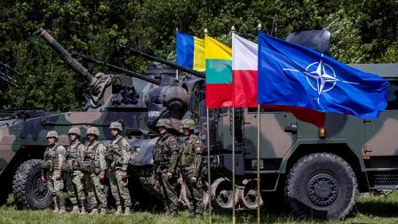 جنود بولنديون ورومانيون يقفون بجوار علم الناتو في قرية شيبليسكي، 7 يوليو 2022 (فرانس برس)
